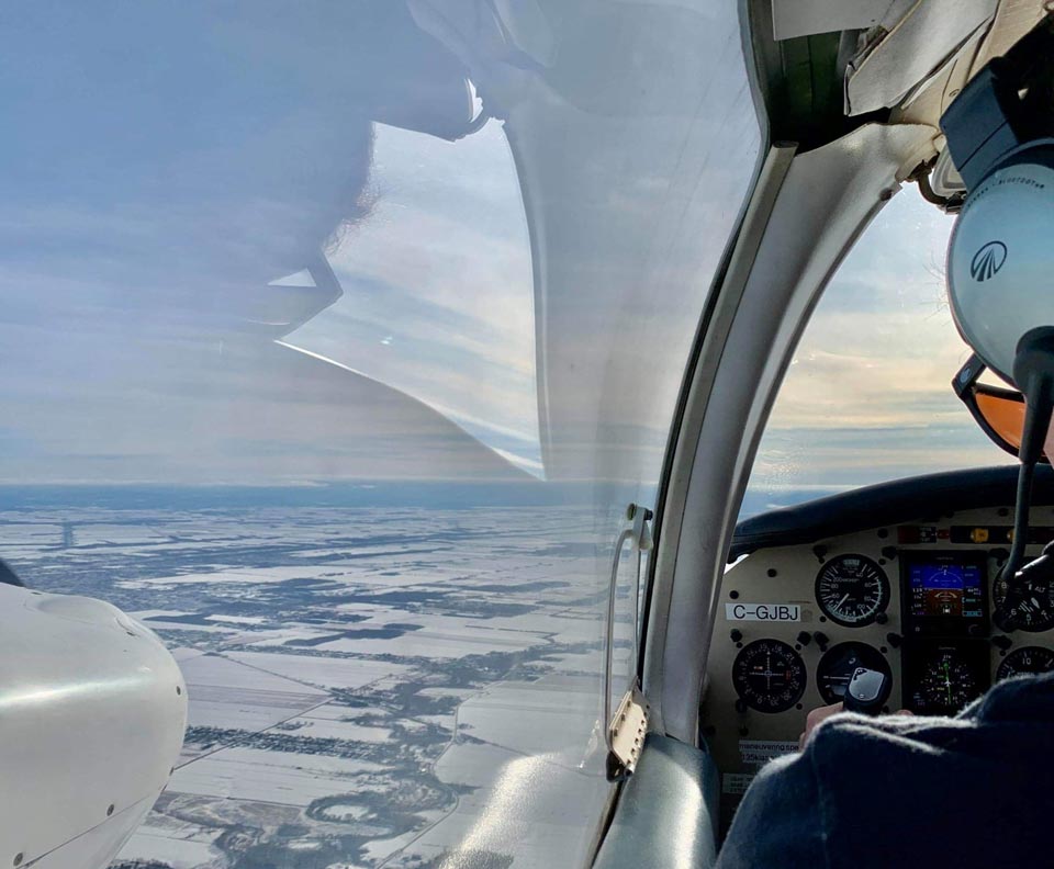 pilote d'un avion bi-moteur à hélice en vol regardant la terre de sa fenêtre